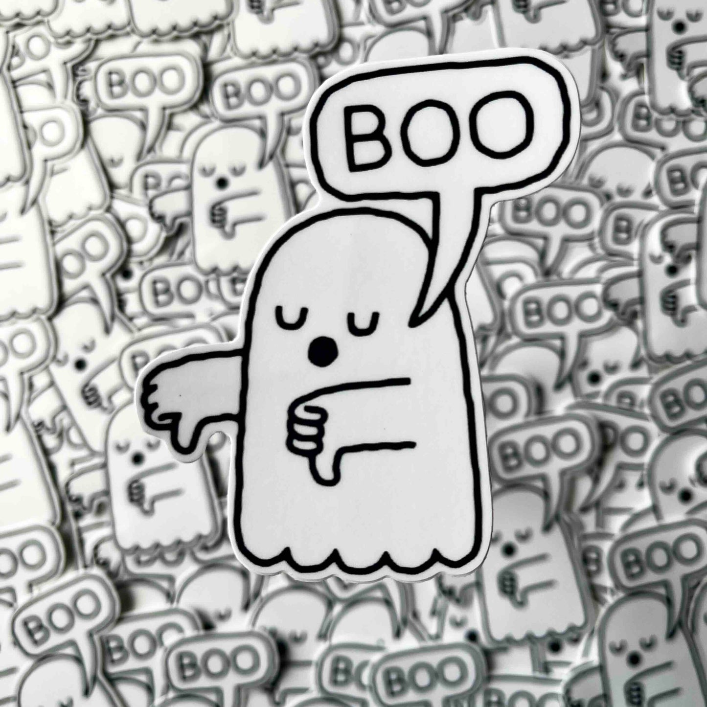 A single cartoon ghost sticker or patch with a speech bubble reading “BOO” is centered over a dense background of many identical ghost motifs in grayscale.
