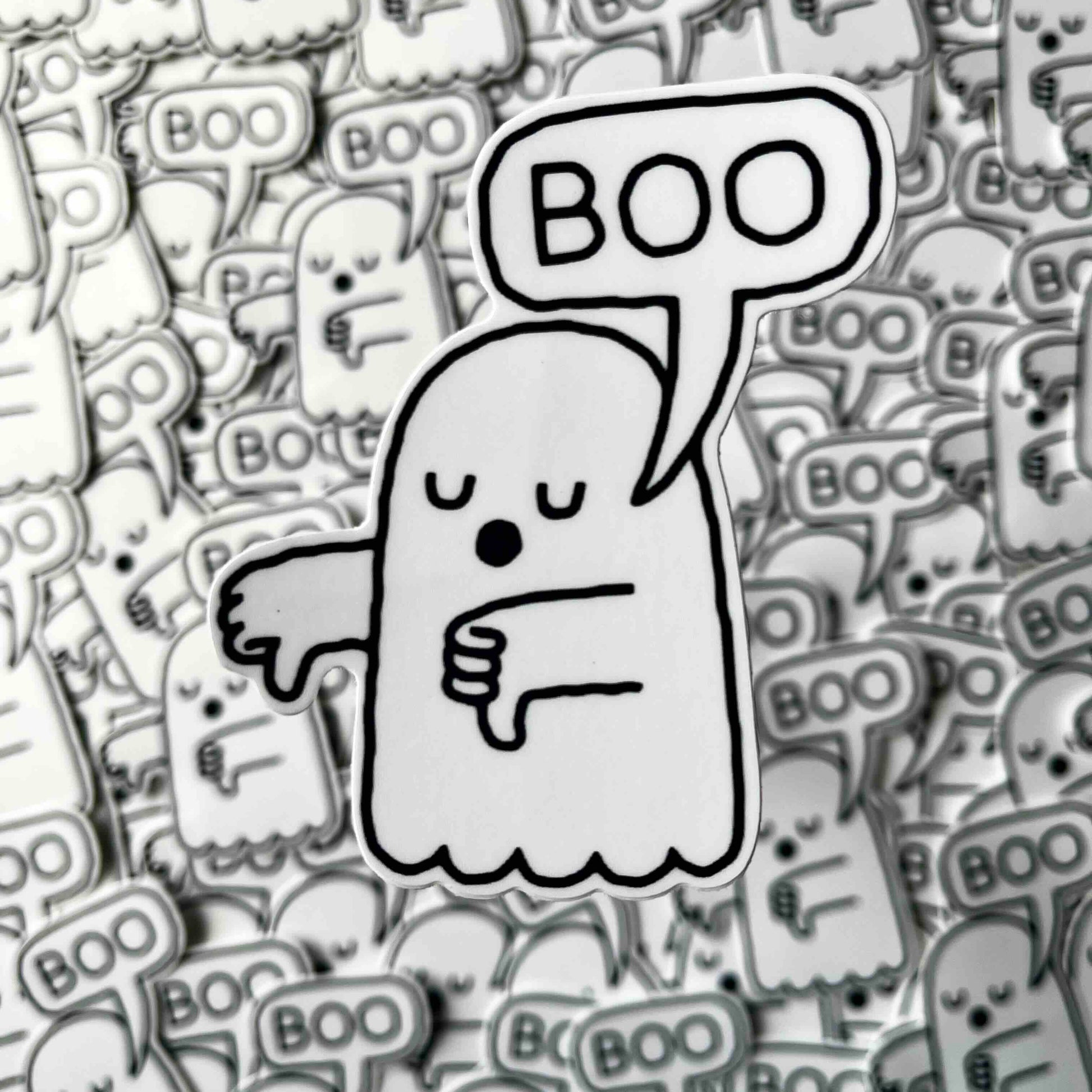 A single cartoon ghost sticker or patch with a speech bubble reading “BOO” is centered over a dense background of many identical ghost motifs in grayscale.
